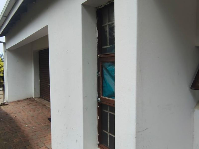 Rear exterior view of the property featuring brick paving, a roller shutter door, and window frames showing signs of wear and maintenance needs.