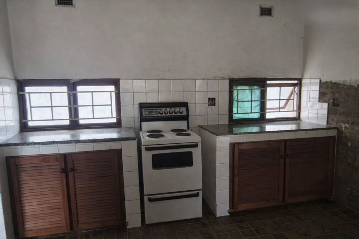 A dated kitchen featuring wooden cabinetry, stone countertops, and a freestanding electric stove, requiring renovation to address wall and floor finish deterioration.