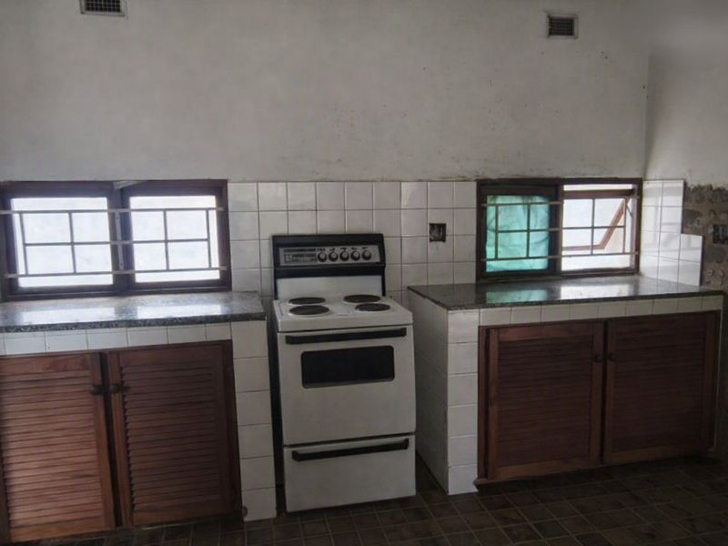 A dated kitchen featuring wooden cabinetry, stone countertops, and a freestanding electric stove, requiring renovation to address wall and floor finish deterioration.