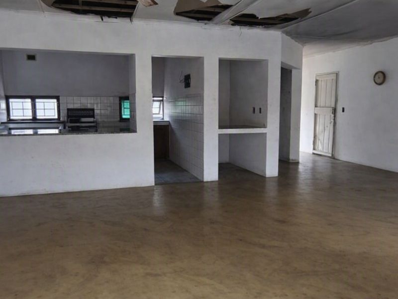 An open-plan living and kitchen area featuring a basic layout, tiled kitchen surfaces, and significant ceiling damage requiring repair.