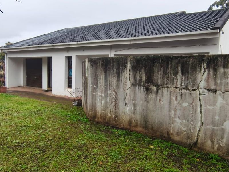 Rear view of the property featuring a lawn area and a concrete boundary wall showing signs of structural cracking and weathering.