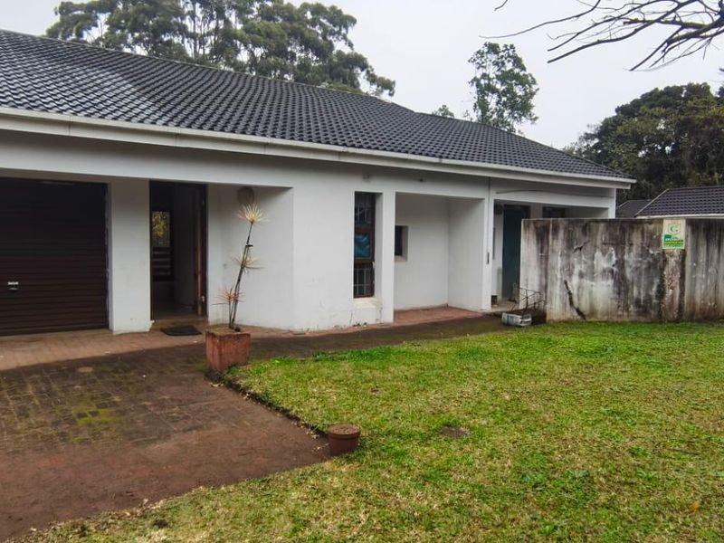 Front elevation of a single-story house featuring a tiled roof, integrated garage, and a paved driveway with an adjacent lawn and boundary wall.