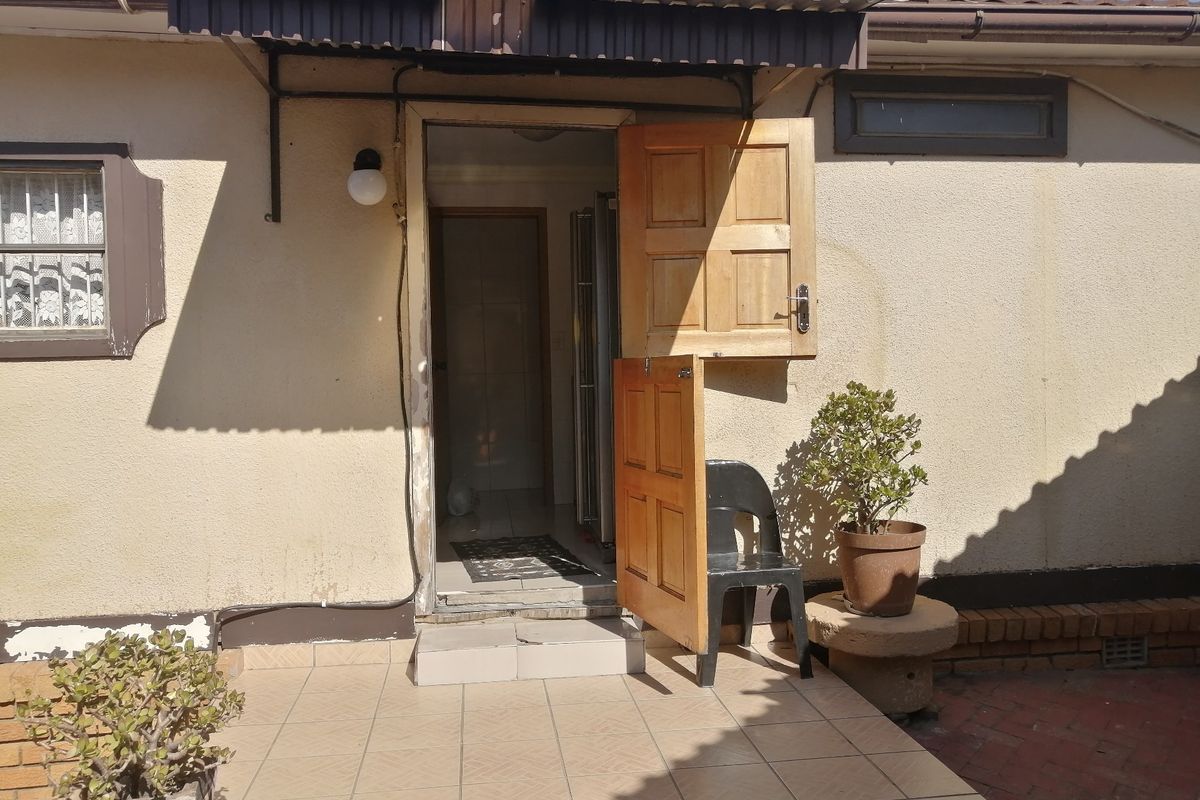 Rear exterior view featuring a tiled patio area, a wooden stable door, and a protective awning over the entrance.