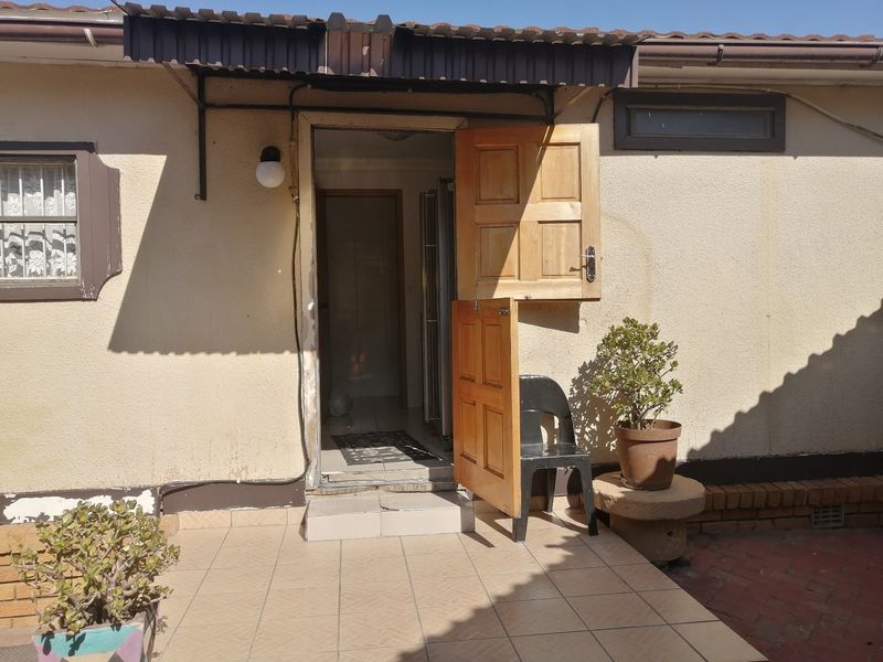 Rear exterior view featuring a tiled patio area, a wooden stable door, and a protective awning over the entrance.