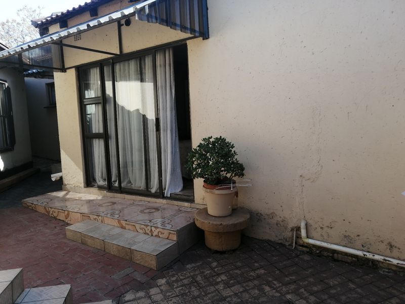 Rear exterior view featuring a sliding glass door, tiled entrance steps, and a paved courtyard area with visible wall plaster damage.