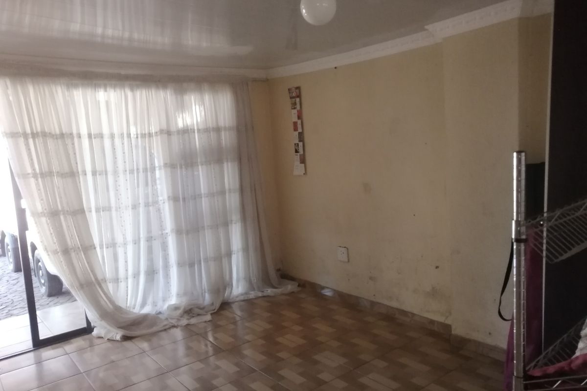 An empty living room featuring tiled flooring and a large sliding glass door providing natural light and access to the exterior.