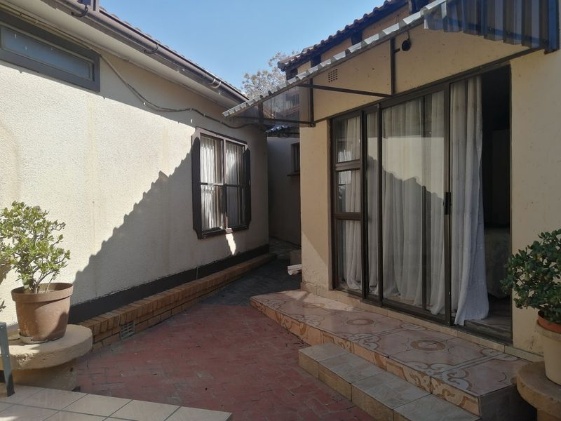 A rear exterior view featuring a tiled patio area, sliding glass doors, and a brick-paved walkway between building sections.