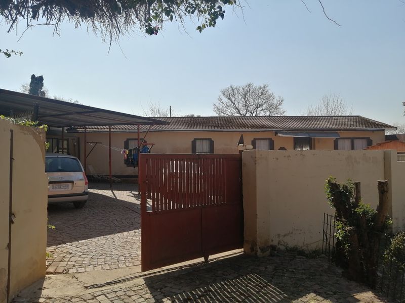 Front exterior view of the property featuring a paved driveway, carport, and gated entrance with boundary walls.