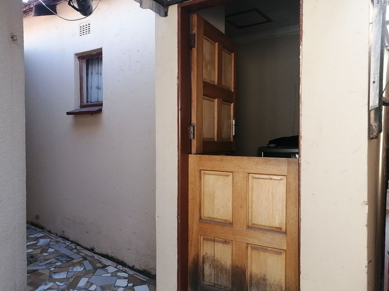 A rear exterior view featuring a wooden stable door and a tiled pathway along the side of the building.