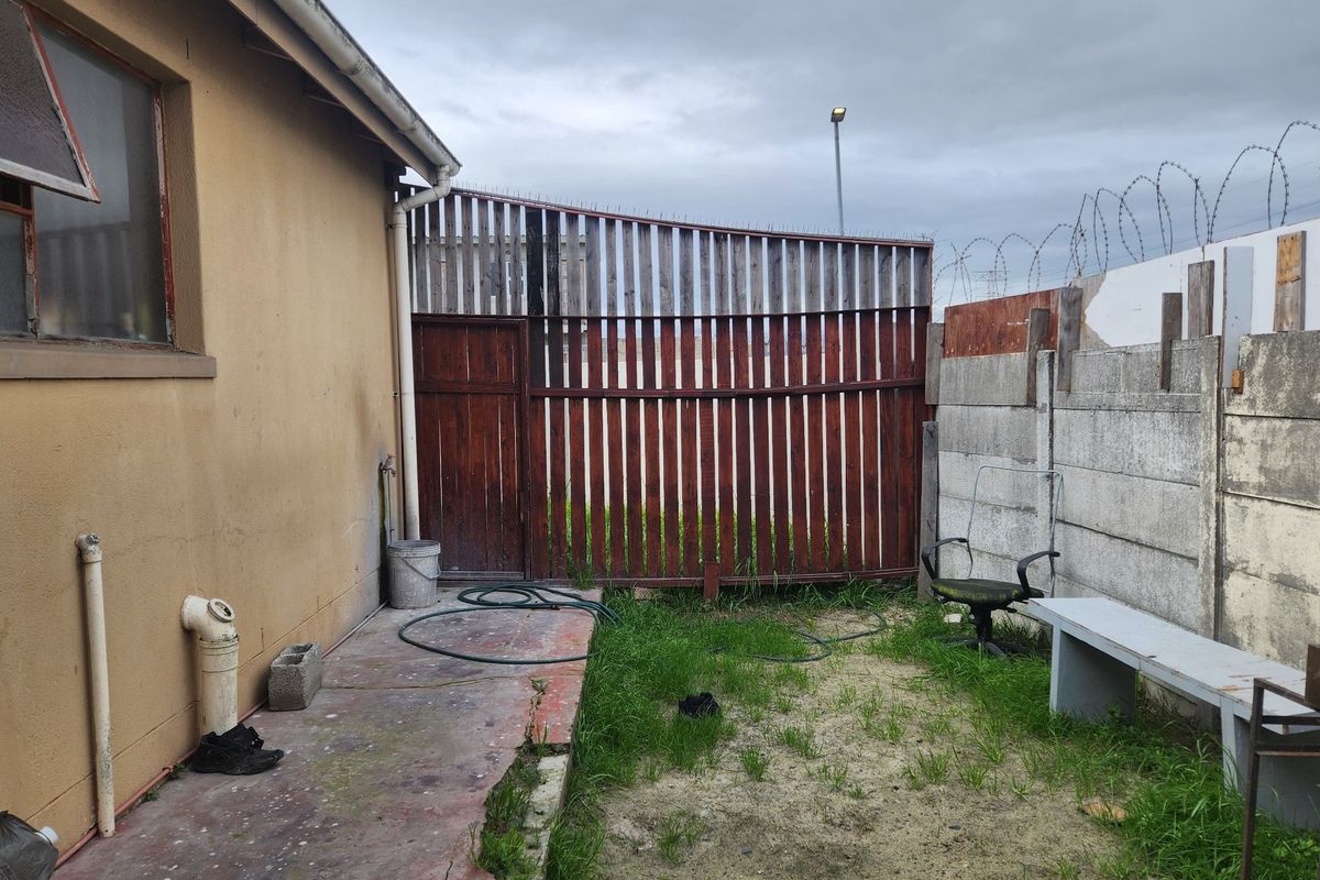 A rear exterior area featuring a concrete pathway, precast concrete boundary wall with razor wire, and timber fencing, requiring maintenance and landscaping.