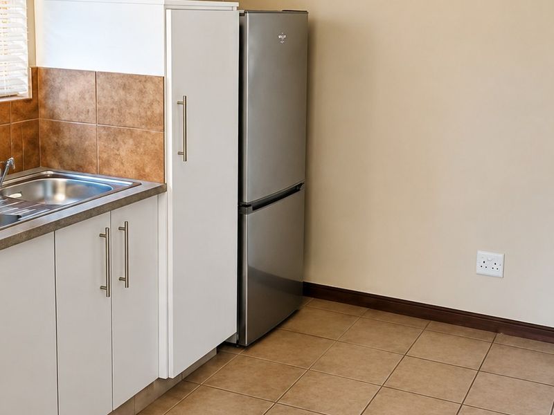 A clean kitchen area featuring tiled flooring, built-in cabinetry with a stainless steel sink, and a wall-mounted air conditioning unit.
