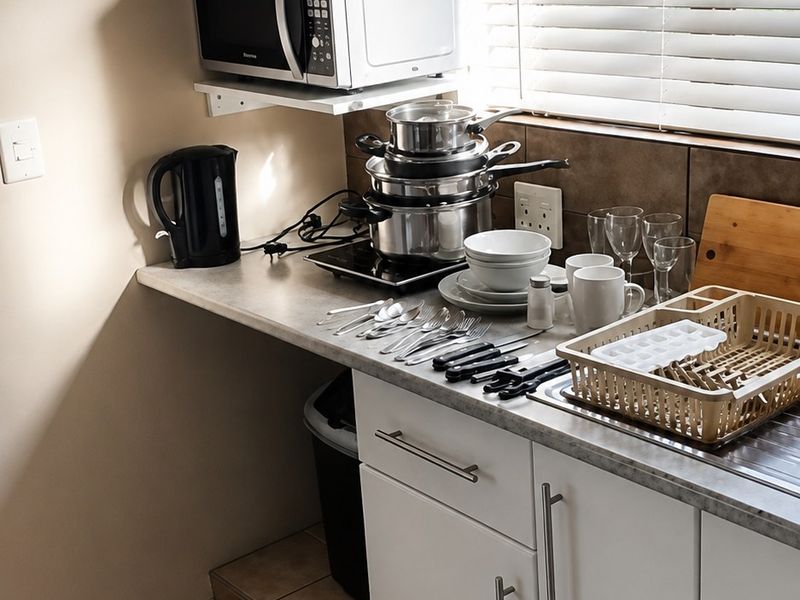 A functional kitchen corner featuring white cabinetry, laminate countertops, tiled flooring, and a window with venetian blinds.
