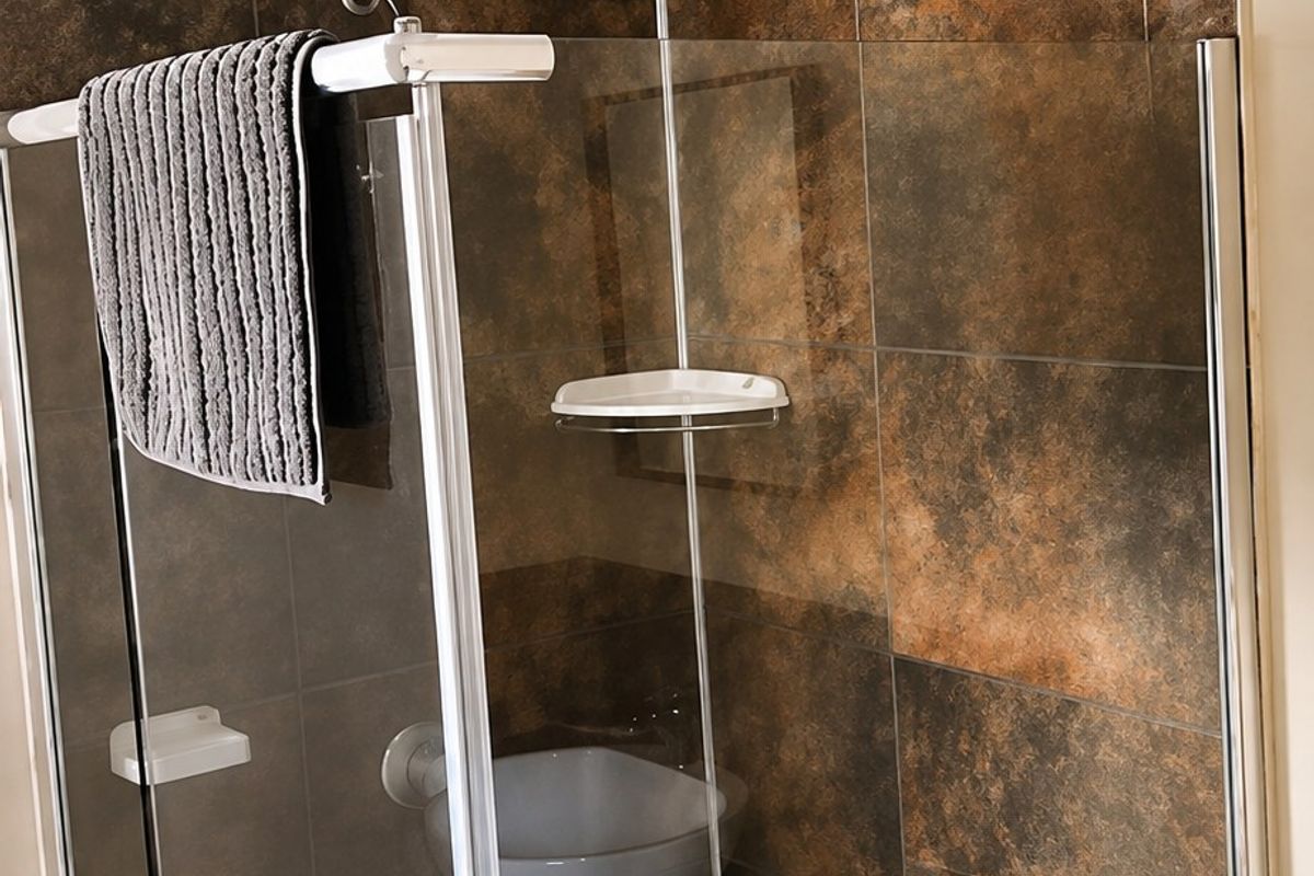 A modern bathroom shower featuring dark textured wall tiles, a glass enclosure, and a built-in corner shelf.