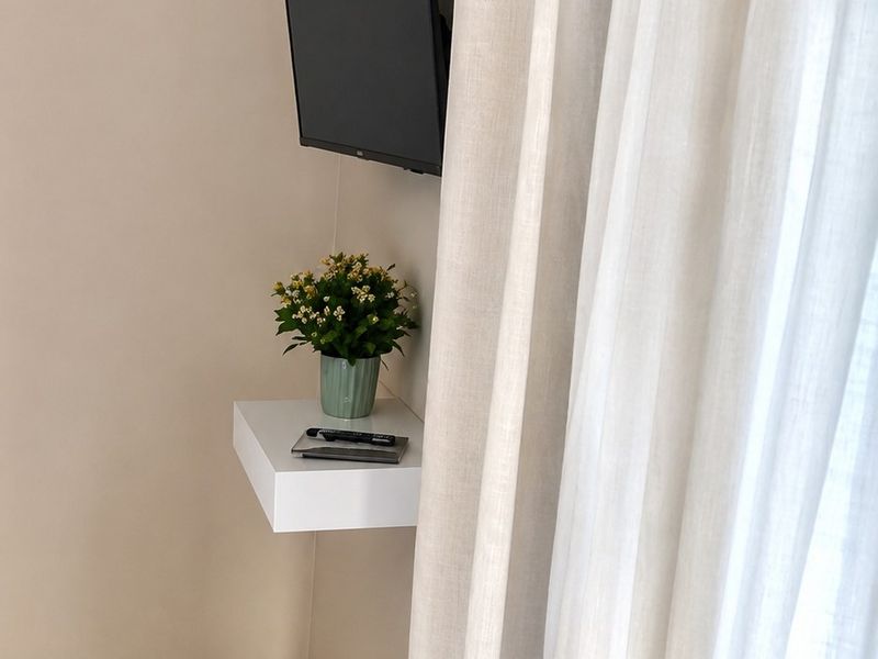 A corner view of a room featuring ceramic tiled flooring, decorative cornice, and a wall-mounted shelf with a security sensor installed.