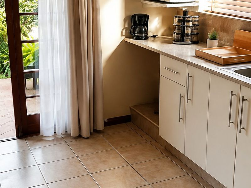 A functional kitchen area featuring white cabinetry, tiled flooring, and direct access to an outdoor patio through a glass panel door.