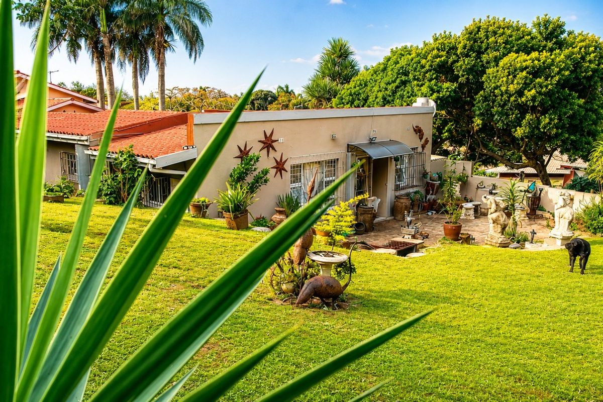 Rear view of the property featuring a paved patio area, tiled roof, and established garden space.