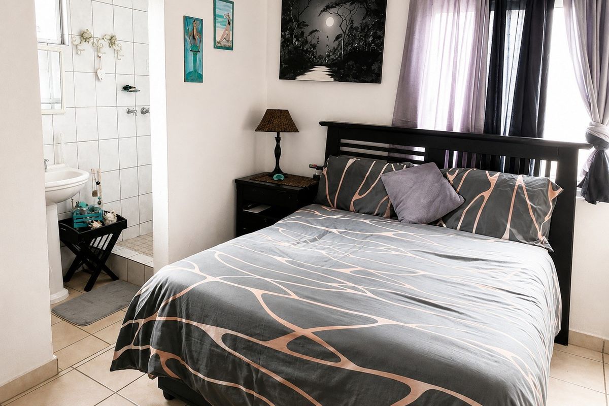 A bedroom featuring an open-plan en-suite bathroom with a pedestal basin and tiled shower area, finished with neutral ceramic floor tiles.