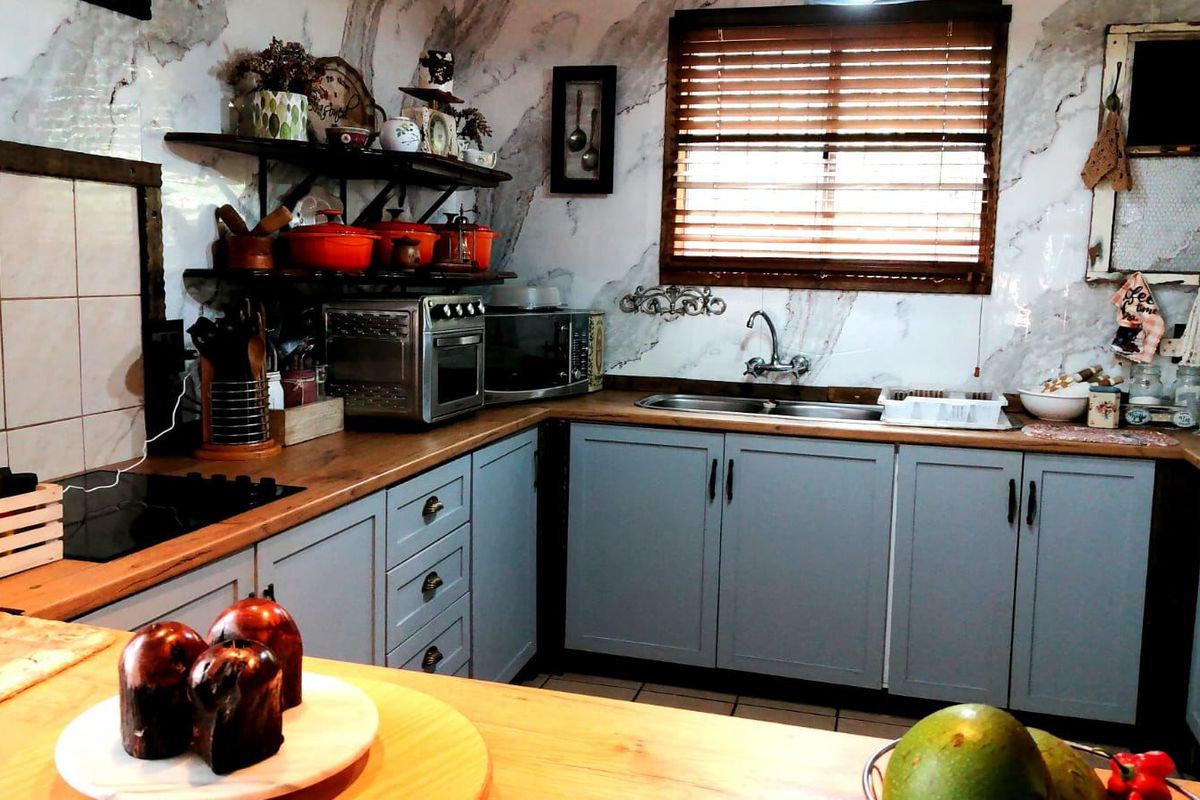 A well-maintained kitchen featuring shaker-style cabinetry, wooden countertops, marble-effect wall tiles, and a double basin sink with a window view.