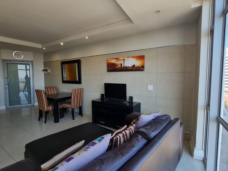 Open-plan living area featuring tiled floors, recessed lighting, and large windows with city views, seamlessly integrating a compact kitchen space.