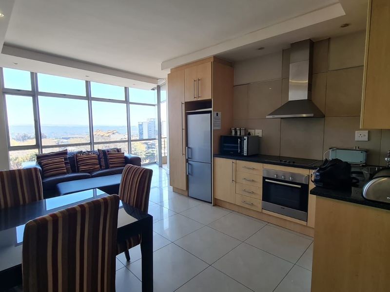 Open-plan living and kitchen area featuring modern cabinetry, built-in appliances, tiled flooring, and expansive windows offering natural light and scenic views.