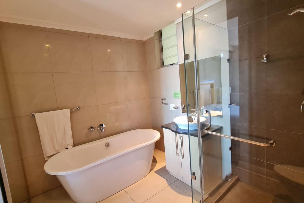 Modern bathroom featuring a freestanding bathtub, a separate glass-enclosed shower, and a vanity with a vessel sink, finished with neutral wall and floor tiles.