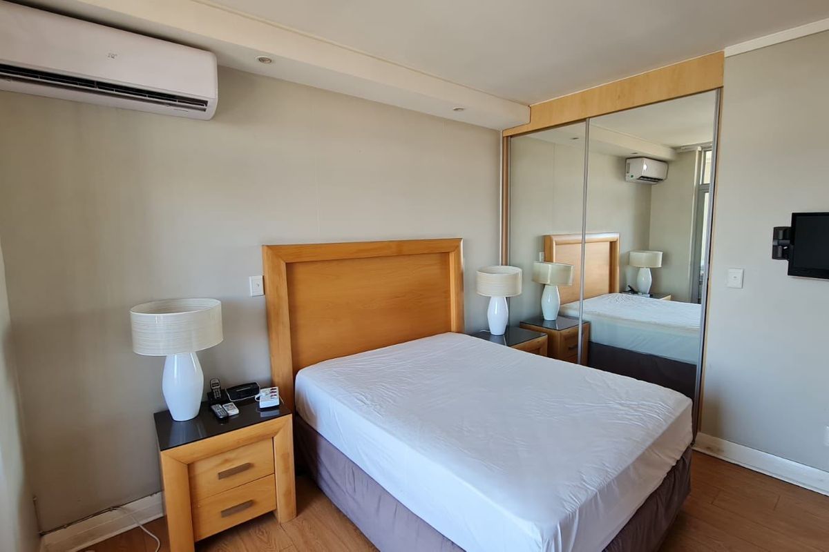 A bedroom featuring laminate flooring, a split-system air conditioner, and large mirrored sliding wardrobe doors providing ample storage.