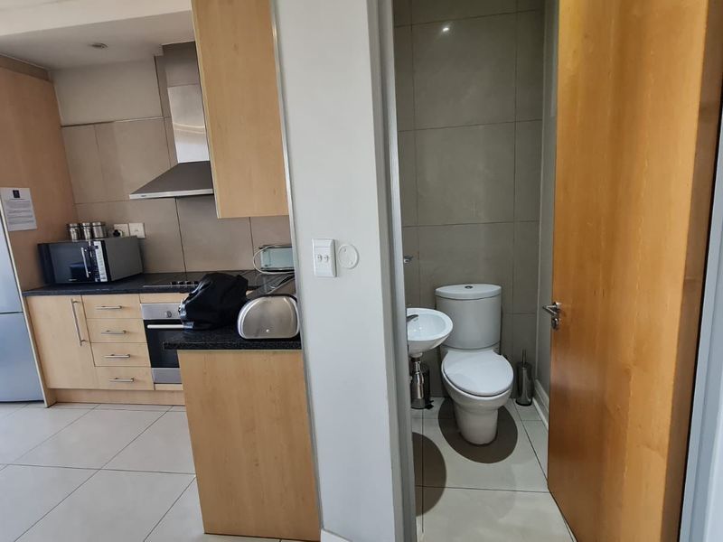 Open plan kitchen with light wood cabinetry and integrated appliances, adjacent to a compact guest bathroom with modern fixtures and tiled finishes.