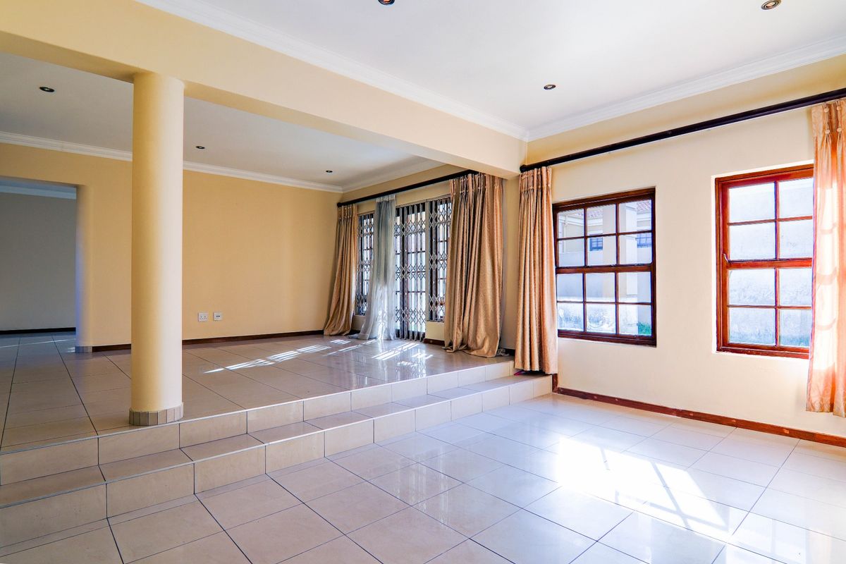 Spacious, light-filled living area featuring a raised platform, tiled flooring, and large timber-framed windows with security gates.