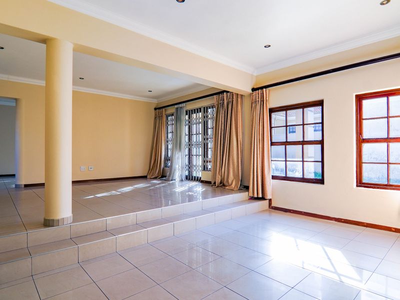 Spacious, light-filled living area featuring a raised platform, tiled flooring, and large timber-framed windows with security gates.