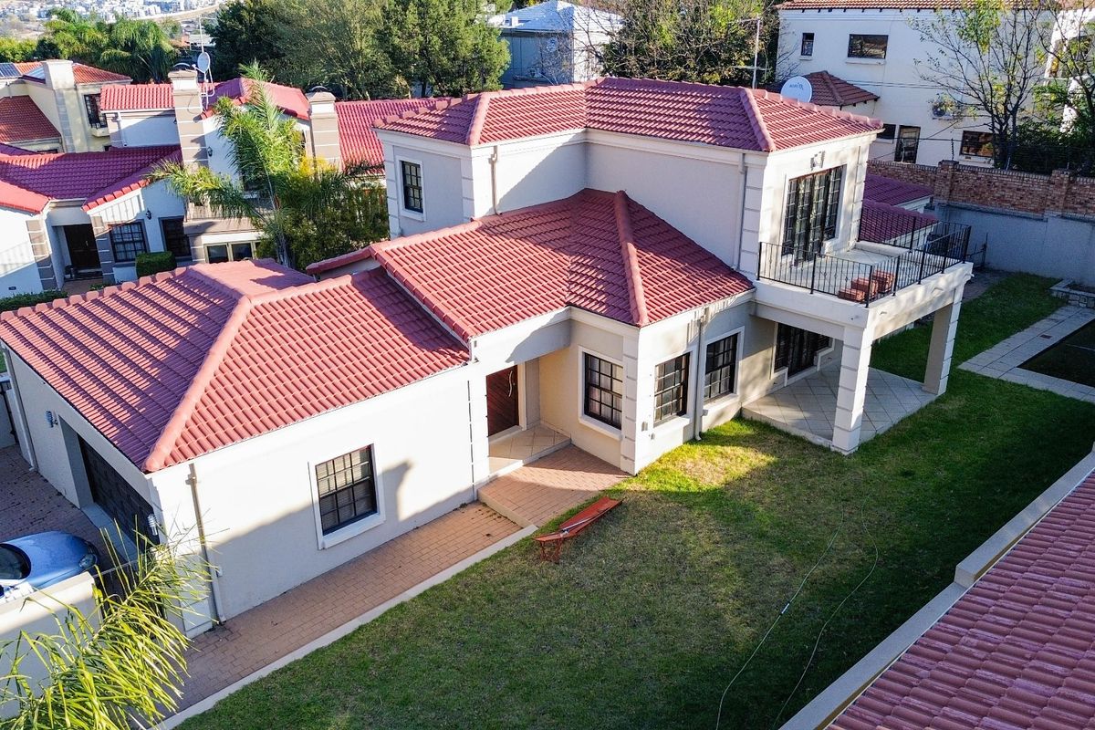Aerial view of a two-story residential property featuring a tiled roof, balcony, paved driveway, garage, and a well-maintained garden area.
