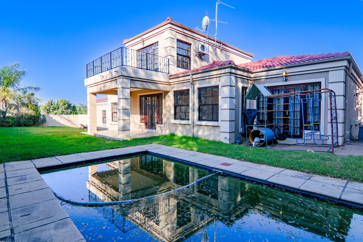 Rear view of the property featuring a swimming pool, paved surround, and an upper-level balcony with wrought iron railings.