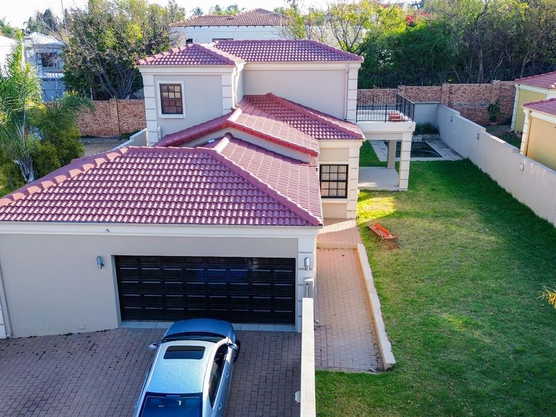 Aerial view of a residential property featuring a tiled roof, paved driveway, garage, and a private garden with boundary walls.