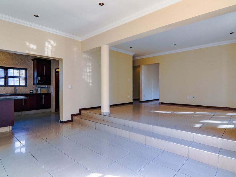 Spacious open-plan living area featuring a raised platform, tiled flooring, and an adjoining kitchen with dark cabinetry and granite countertops.