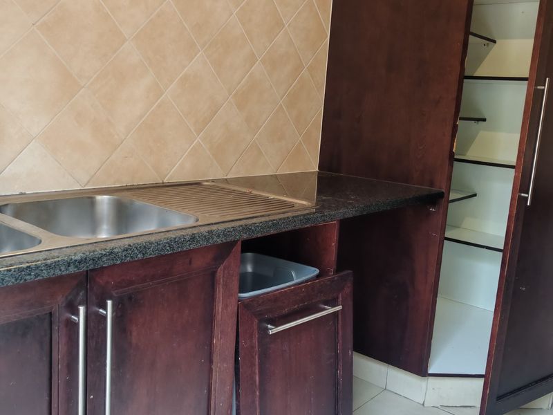 A functional scullery area featuring dark wood cabinetry, granite countertops, a stainless steel sink, and neutral tiled backsplash.