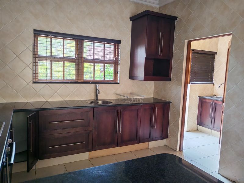A functional kitchen featuring dark wood cabinetry, granite countertops, and a tiled splashback, with an adjacent scullery area visible through the doorway.