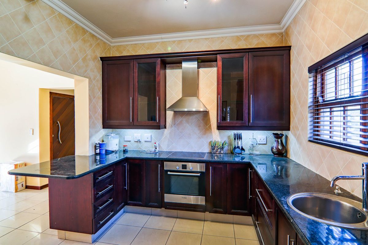 A functional kitchen featuring dark wood cabinetry, granite countertops, stainless steel appliances, and a tiled backsplash with neutral floor tiles.