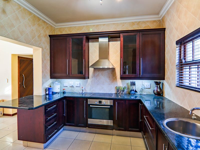 A functional kitchen featuring dark wood cabinetry, granite countertops, stainless steel appliances, and a tiled backsplash with neutral floor tiles.