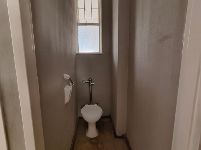 A compact, unfinished bathroom space featuring a standard toilet, tiled flooring, and a window with security bars, requiring cosmetic completion.