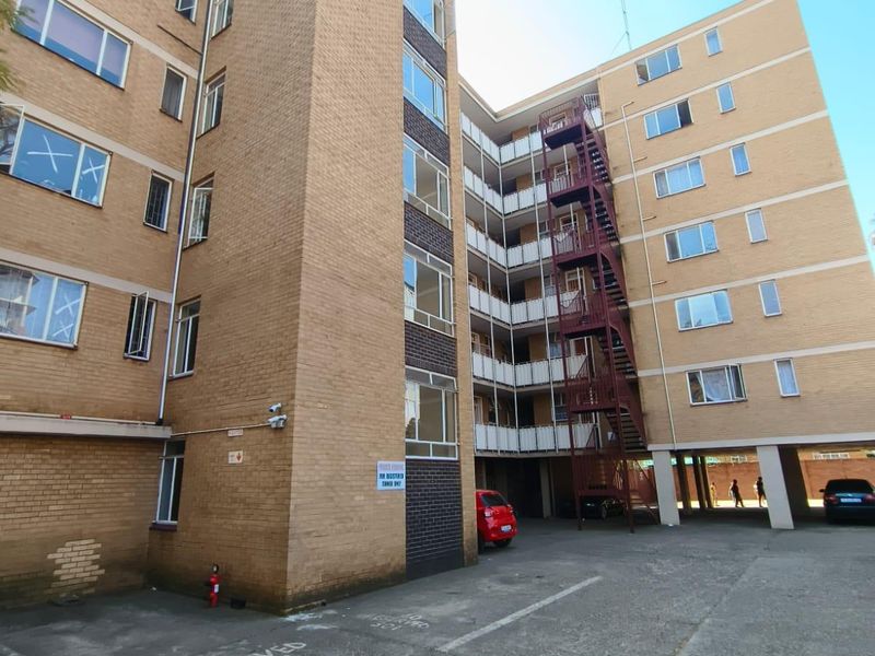 Exterior view of a multi-story brick apartment building featuring an external fire escape staircase and designated parking area.