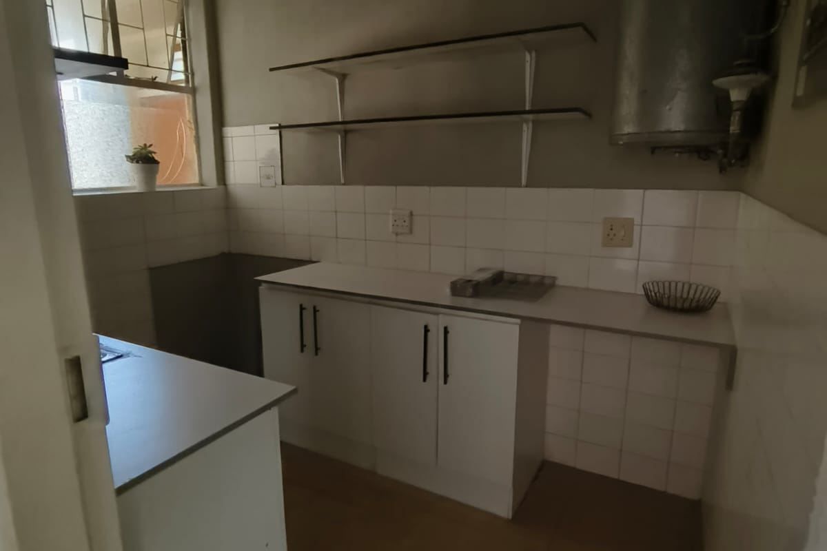 A compact, functional kitchen featuring white cabinetry, tiled splashbacks, and wall-mounted shelving, currently in need of cosmetic updates.