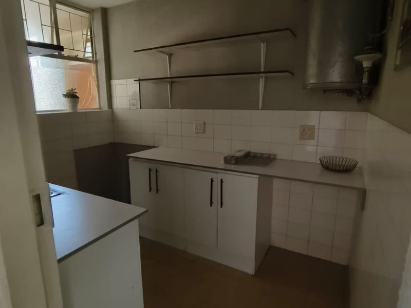A compact, functional kitchen featuring white cabinetry, tiled splashbacks, and wall-mounted shelving, currently in need of cosmetic updates.