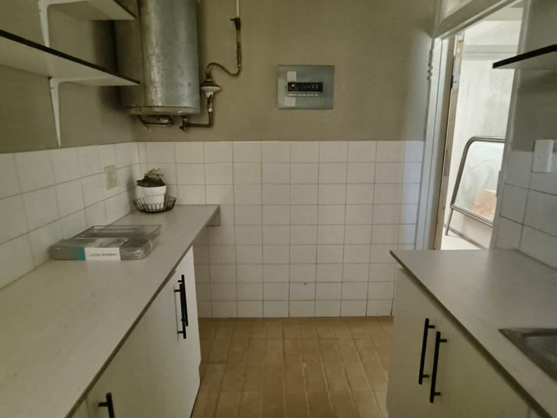 A functional scullery or utility area featuring built-in cabinetry, laminate countertops, tiled splashbacks, and an exposed electric water heater.