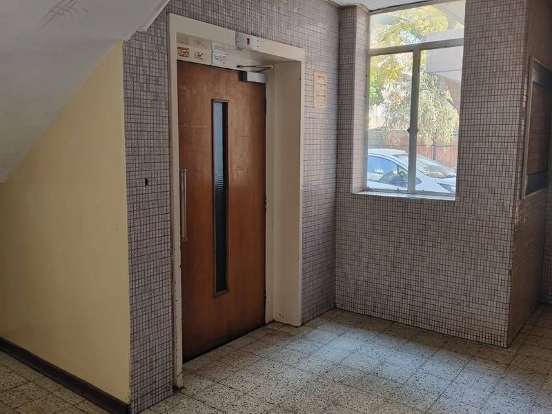 A communal apartment hallway featuring an elevator, tiled flooring, and wall cladding, showing signs of age and wear.