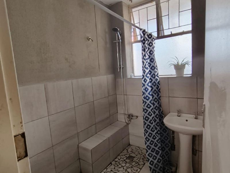 A compact bathroom featuring a pedestal basin and a tiled shower area with unfinished wall surfaces, requiring renovation to improve finishes and overall condition.