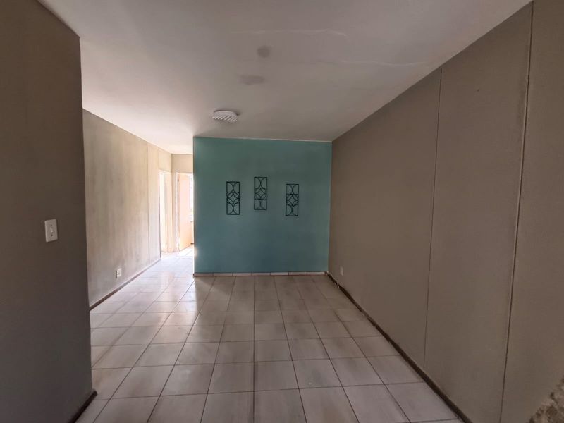 An empty living area featuring tiled flooring and a painted accent wall, offering a blank canvas for potential interior design updates.