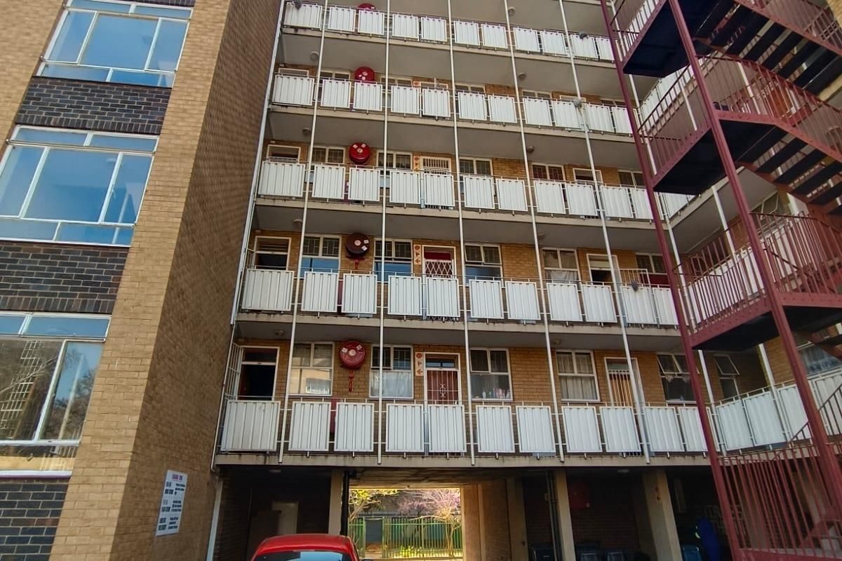 Rear view of a multi-story apartment building featuring brick facade, external metal fire escape staircase, and multiple balconies with fire safety equipment.