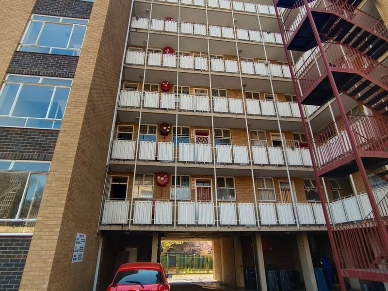 Rear view of a multi-story apartment building featuring brick facade, external metal fire escape staircase, and multiple balconies with fire safety equipment.