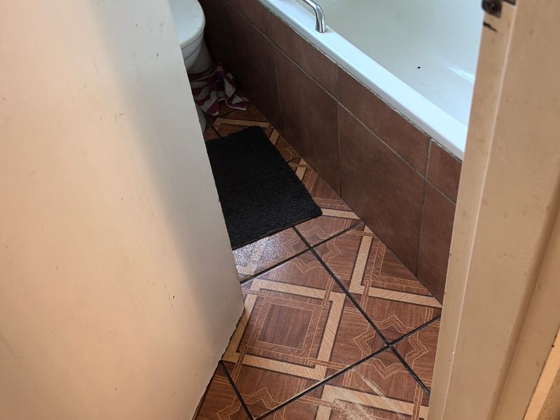 A compact bathroom featuring a bathtub, toilet, and patterned floor tiles. The space is dated and would benefit from modern updates.