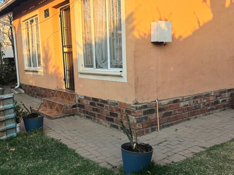 Rear exterior view of the house featuring a brick plinth, paved walkway, and security features on the windows and door.