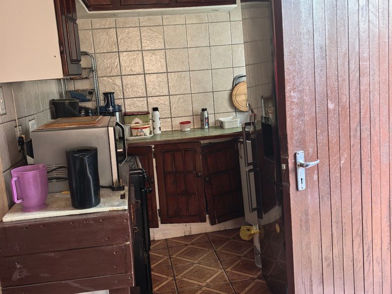 A compact kitchen featuring traditional wooden cabinetry, tiled backsplash, and tiled flooring, currently showing signs of wear and requiring maintenance.